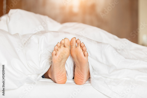 Woman feet under white blanket side view. Beautiful young woman feet with blue pedicure on the bed. Sleeping woman legs under the white blanket