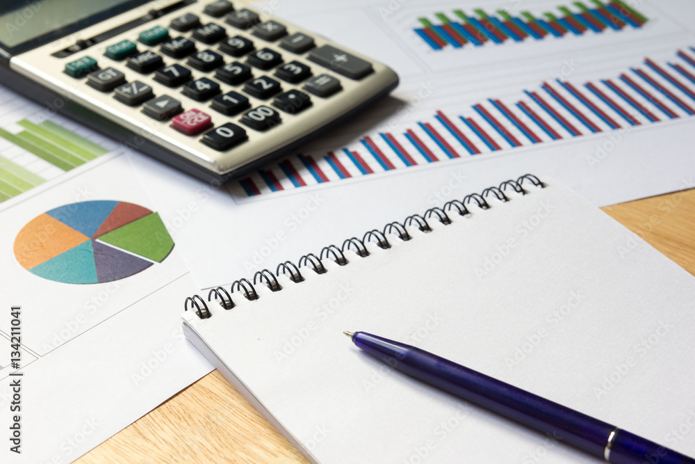 Blank note book with financial graph, calculator and pen backgro
