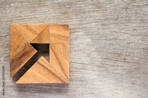Tangram puzzle as arrow in square shape on wooden background (Co