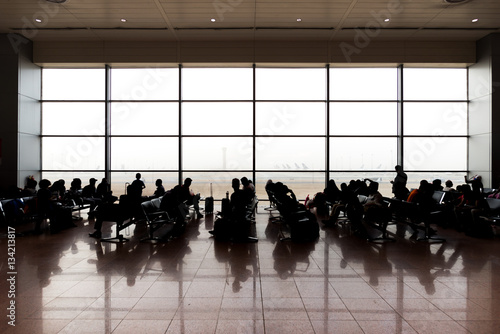 People sitting and waiting for departure in airport terminal. Backlight with big window on aircraft strip.