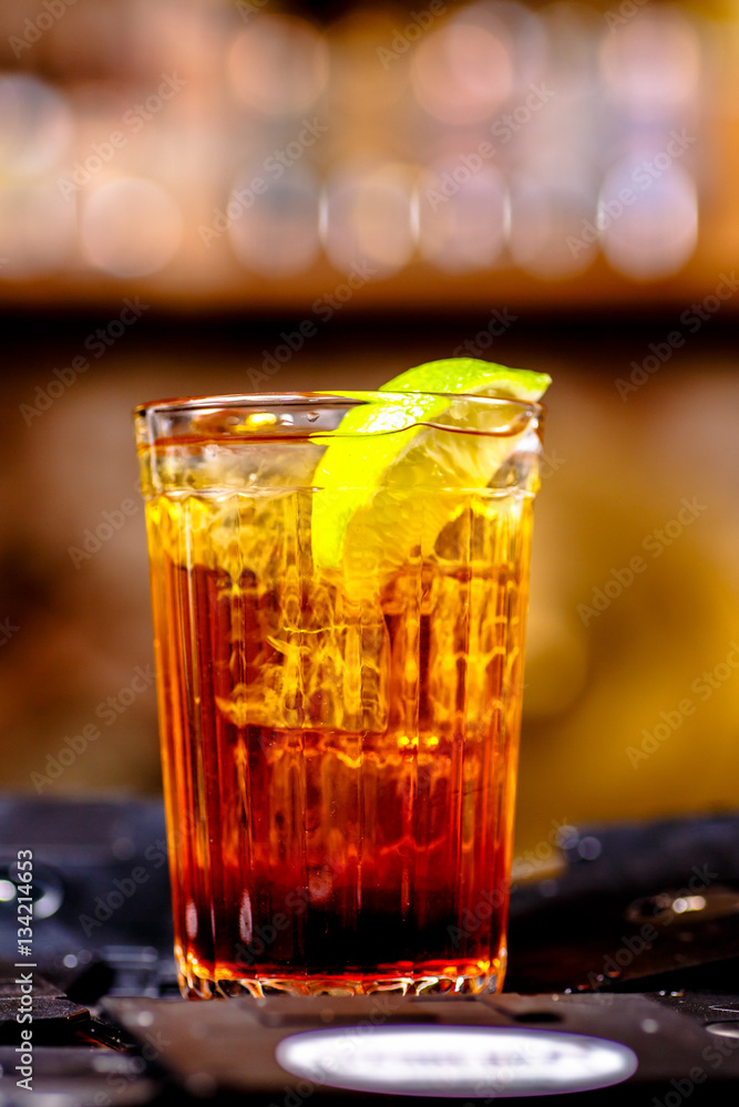 Brown cocktail with a slice of lemon poured into a faceted glass Brown cocktail with a slice of lemon poured into a faceted glass
