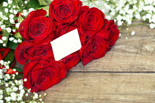 red roses on wooden table with blank white card.