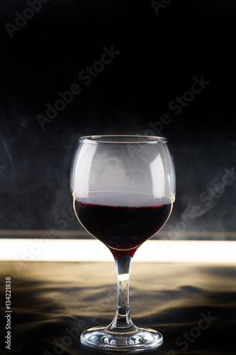 glass of red wine on black background with backlighting and smoke