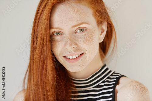 Beauty and skin care. Highly-detailed portrait of attractive redhead teenage girl with charming smile and cute freckles having rest indoors wearing her hair loose. Beautiful woman relaxing at home photo