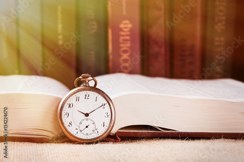 Vintage pocket clock on book against books background with beam of light