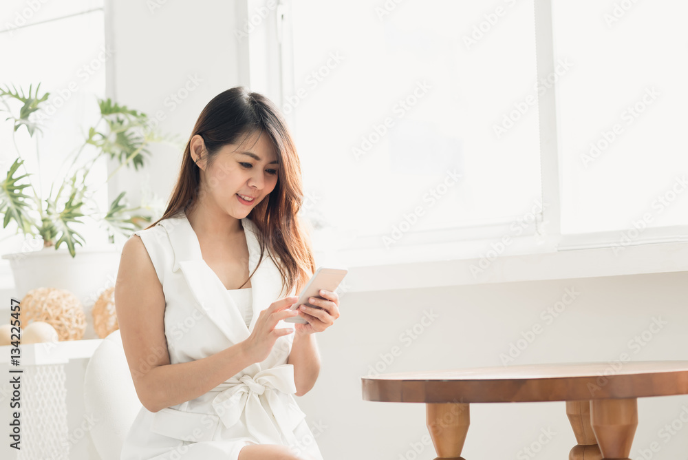 Happy Asian woman smiling while using smart phone in white room Happy Asian woman smiling while using smart phone in white room