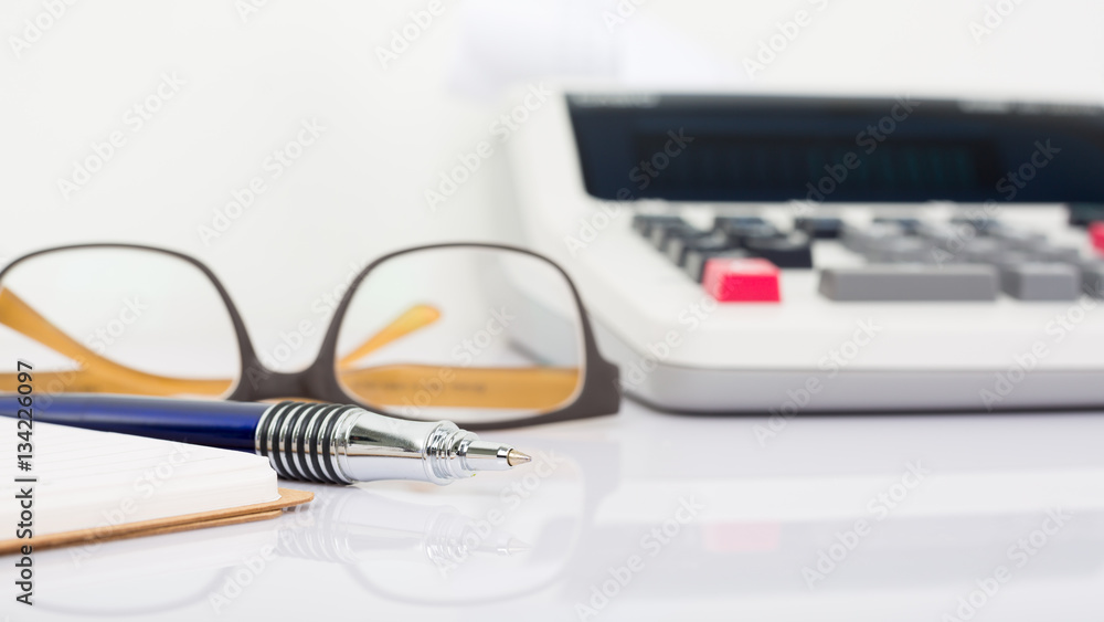 Close up of pen with calculator printed and glasses on white bac Close up of pen with calculator printed and glasses on white bac
