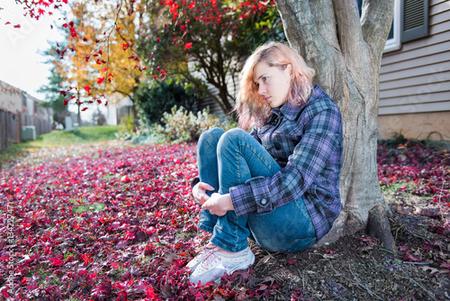 Young woman sitting by tree in autumn red maple leaves foliage i