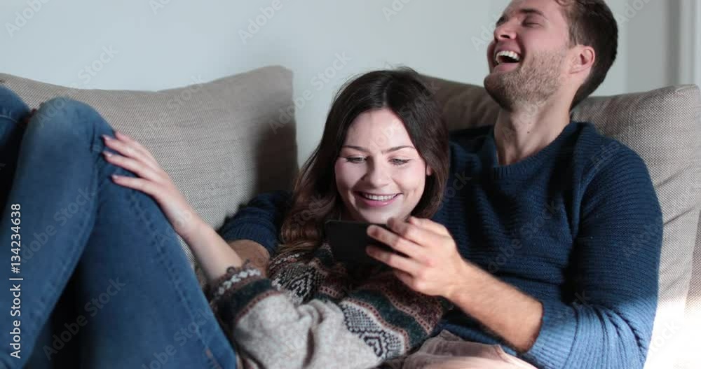 Couple relaxing on sofa at home watching video on smartphone Couple relaxing on sofa at home watching video on smartphone
