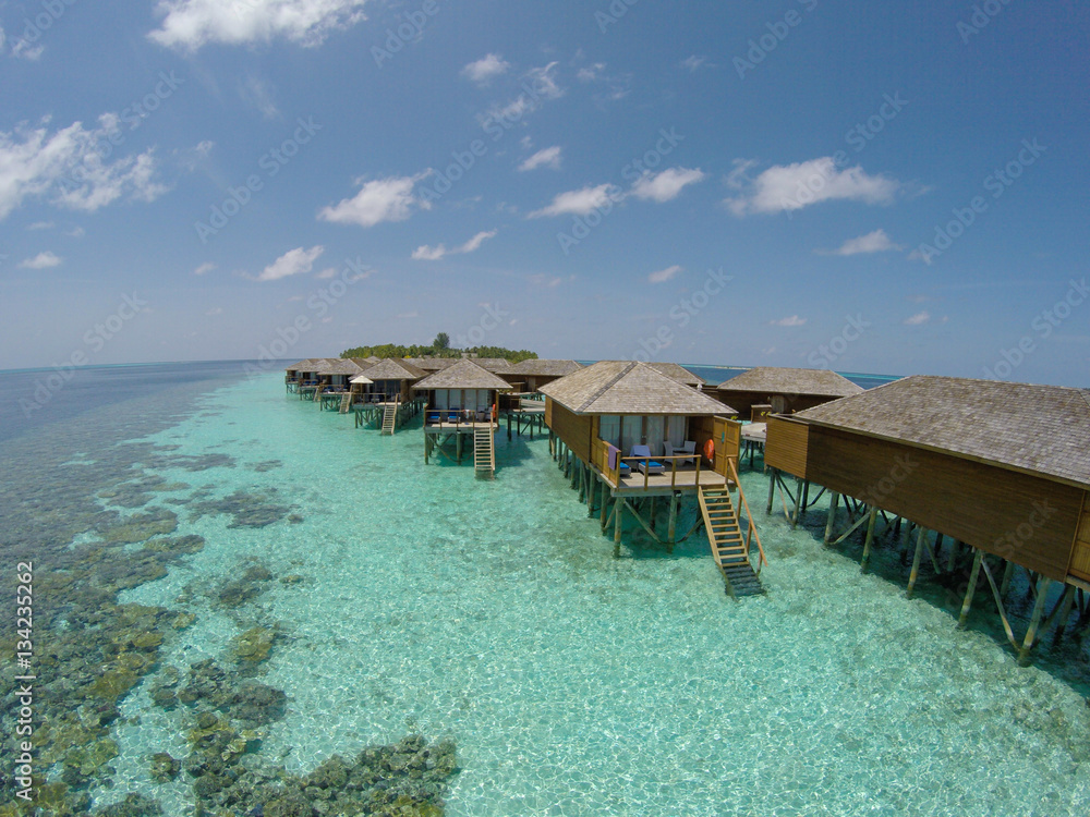 Fototapeta premium Aerial view of a tropical island in turquoise water. Luxurious over-water villas on tropical island resort maldives for holiday vacation background concept -Boost up color Processing.