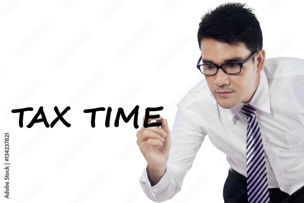 Male entrepreneur writes tax time on whiteboard Male entrepreneur writes tax time on whiteboard