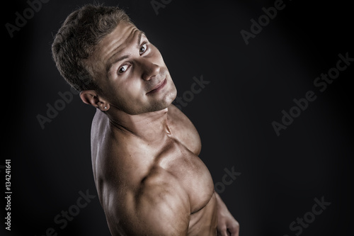 Handsome shirtless bodybuilder shot from above, standing on dark background