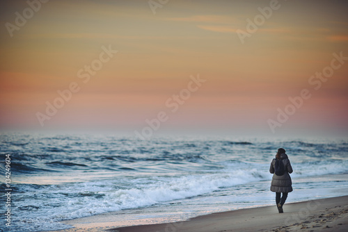 Fotografi Girl walking in the empty beach, sunset time. Baltic sea