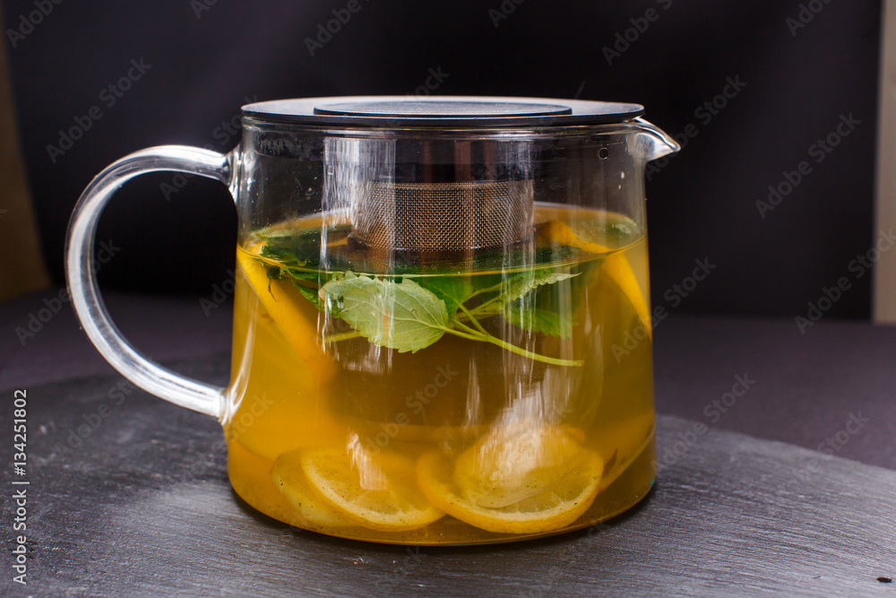 hot tea with mint and lemon in a glass pot on black background hot tea with mint and lemon in a glass pot on black background