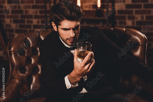 Portrait of handsome young man holding glass of cognac photo