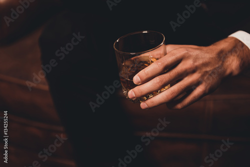 Close up of man's hand holding class of whiskey