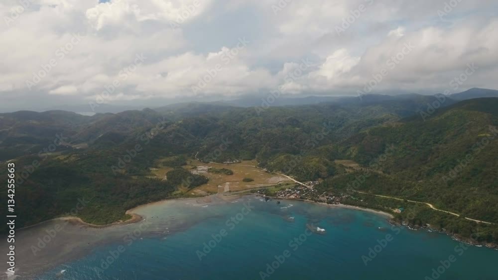 The coast of the tropical island with the mountains and the rainforest on a background of ocean with big waves.Aerial view: sea and the tropical island with rocks, beach and waves. Seascape: sky The coast of the tropical island with the mountains and the rainforest on a background of ocean with big waves.Aerial view: sea and the tropical island with rocks, beach and waves. Seascape: sky