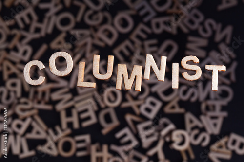 Columnist wooden letters created in wood floating above random letters below out of focus on a black background