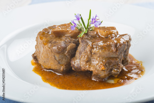 Guiso de carne de rabo de toro o ternera con salsa de verduras y vino tinto decorado con flores de romero para la comida photo