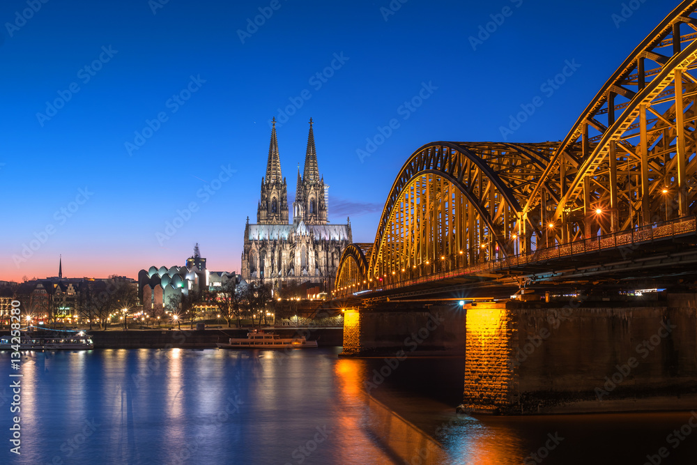 Cologne Cathedral and Hohenzollern Bridge at nighttime.