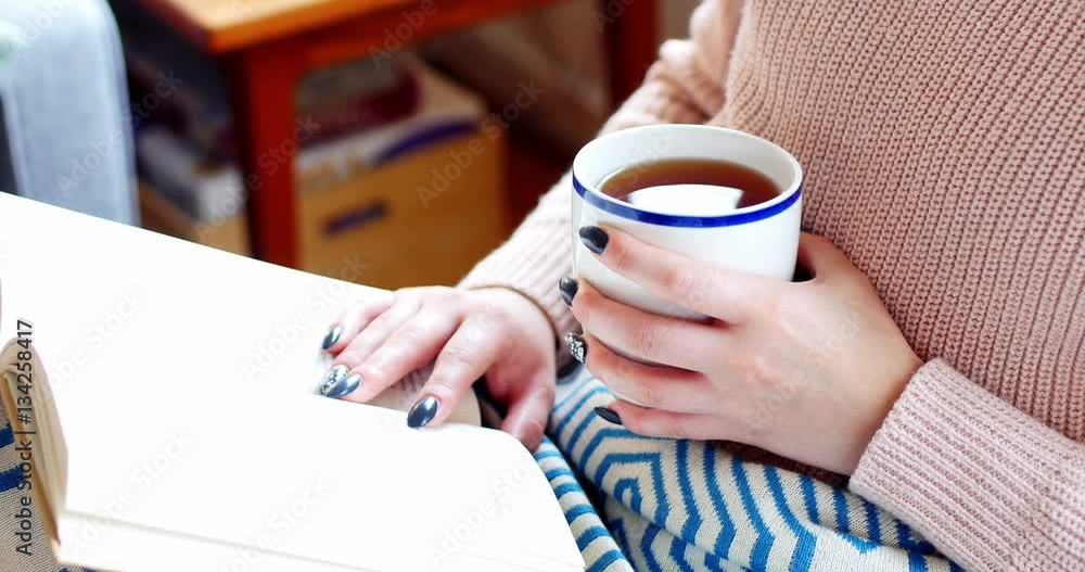 Woman reading a novel while having coffee in living room Woman reading a novel while having coffee in living room