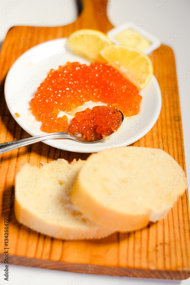 Red caviar, lemon and bread on wooden board white table background Red caviar, lemon and bread on wooden board white table background