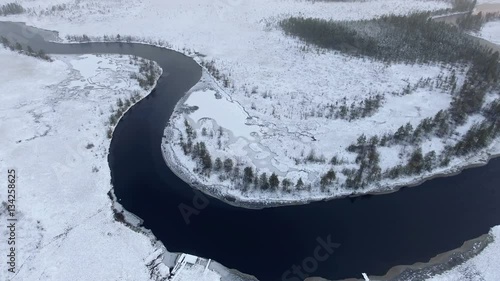 Winter river bend with open water flowing in snowy swamplands of Karelia. Aerial view from flying drone. Russia
