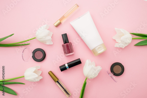 Flat lay, top view table desk frame. Feminine desk workspace with cosmetics, lipstick and tulip flowers on pink background. Valentine's background.