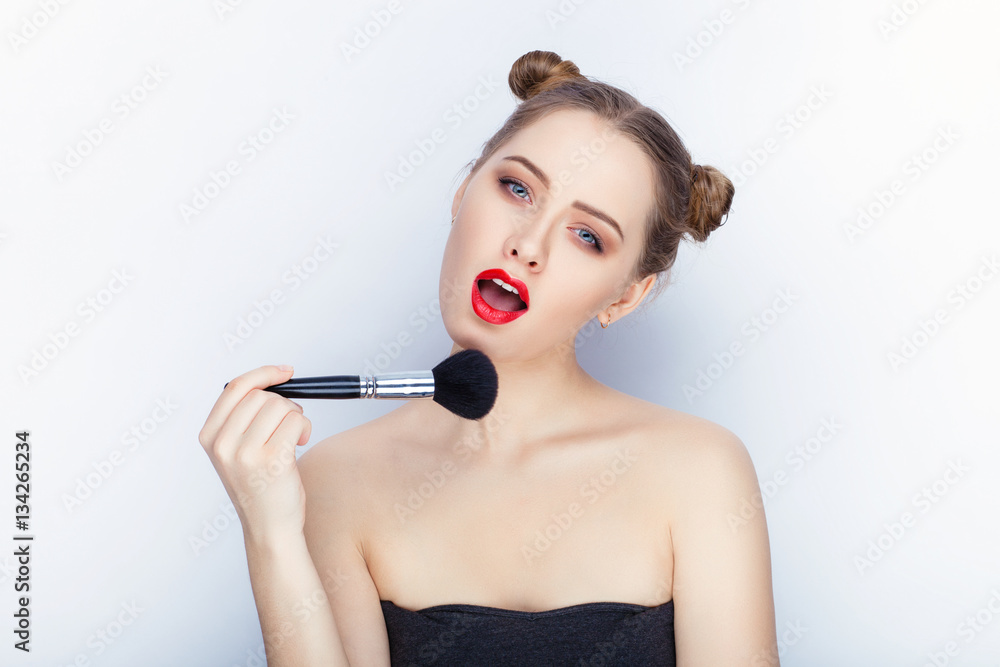 Young pretty woman trendy makeup bright red lips bun hairstyle bare shoulders act the ape with brush white studio background Young pretty woman trendy makeup bright red lips bun hairstyle bare shoulders act the ape with brush white studio background