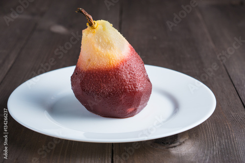 one poached pear on white plate on dark wooden background