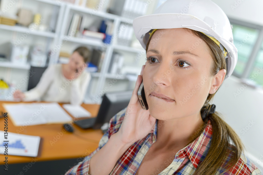 Lady wearing hardhat, on cellphone biting lip Lady wearing hardhat, on cellphone biting lip