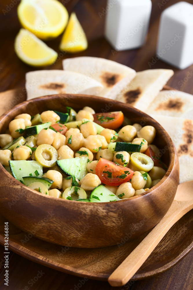 Salat aus Kichererbsen, grünen Oliven, Gurken, Kirschtomaten und Petersilie in Holzschüssel serviert, fotografiert mit natürlichem Licht (Selektiver Fokus, Fokus ein Drittel in den Salat) Salat aus Kichererbsen, grünen Oliven, Gurken, Kirschtomaten und Petersilie in Holzschüssel serviert, fotografiert mit natürlichem Licht (Selektiver Fokus, Fokus ein Drittel in den Salat)