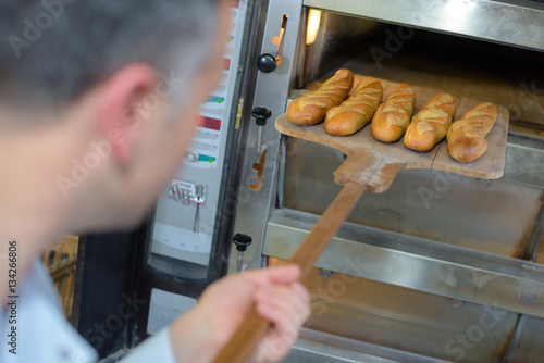 baker getting fresh bread out of the traditional oven photo