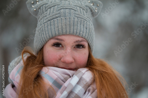 Young woman in winter park standing on alley, wrapped in a scarf and looking to camera