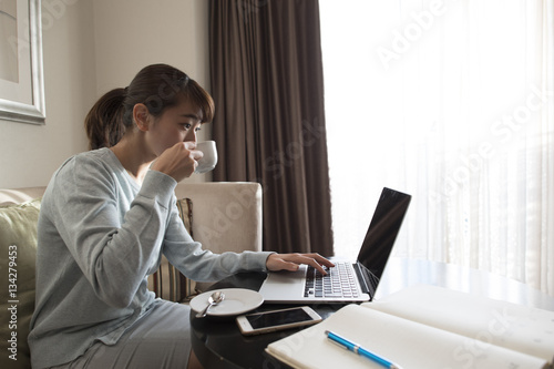 A woman is working on a laptop while drinking coffee