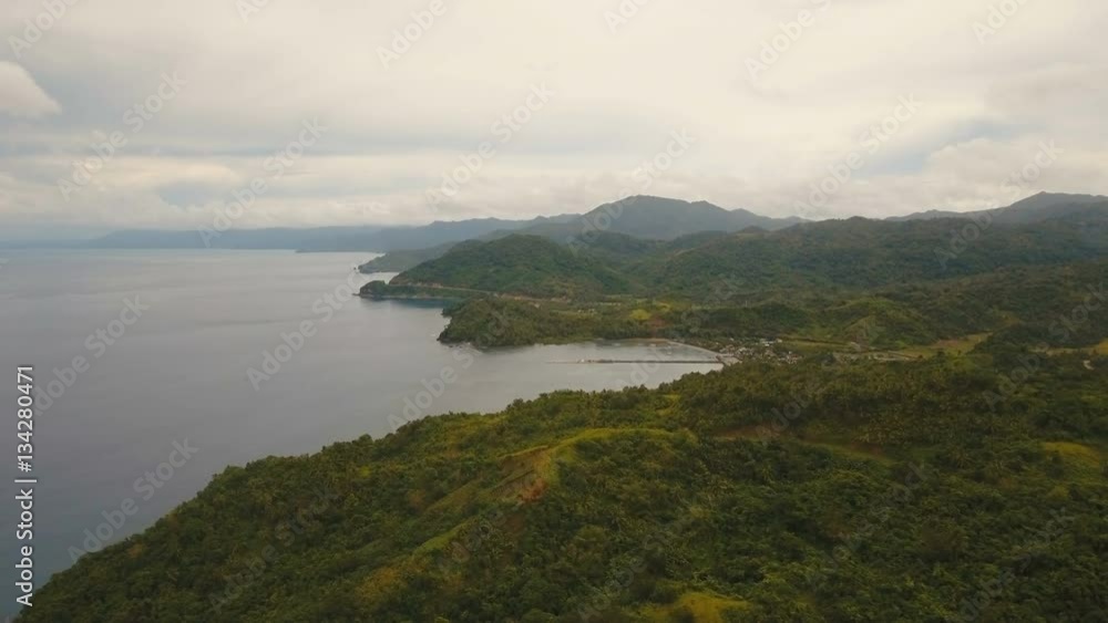 The coast of the tropical island with the mountains and the rainforest on a background of ocean with big waves.Aerial view: sea and the tropical island with rocks, beach and waves. Seascape: sky The coast of the tropical island with the mountains and the rainforest on a background of ocean with big waves.Aerial view: sea and the tropical island with rocks, beach and waves. Seascape: sky