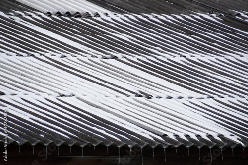 Close up of dark gray corrugated metal roof with snow in the trough and icicles on the eaves. 