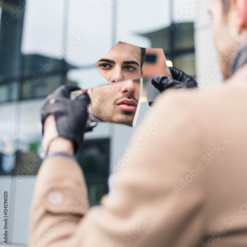 Beautiful young man looking at himself in a shattered mirror