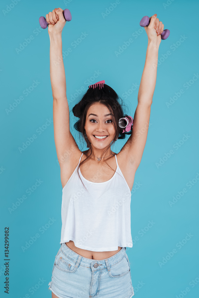 Happy young lady with hair curlers holding dumbbells Happy young lady with hair curlers holding dumbbells