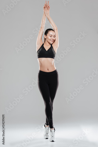 Smiling beautiful young sportswoman with raised hands standing tiptoes