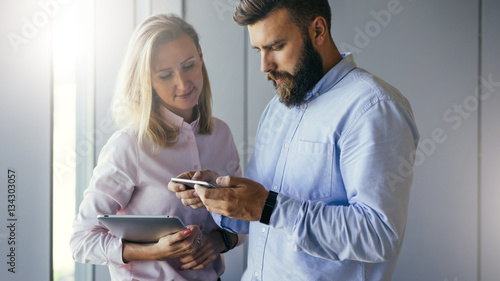Businessman showing business women information on smartphone screen. Woman holding digital tablet and looking on screen of phone. Businessmen discussing business plan. Teamwork, project preparation. photo