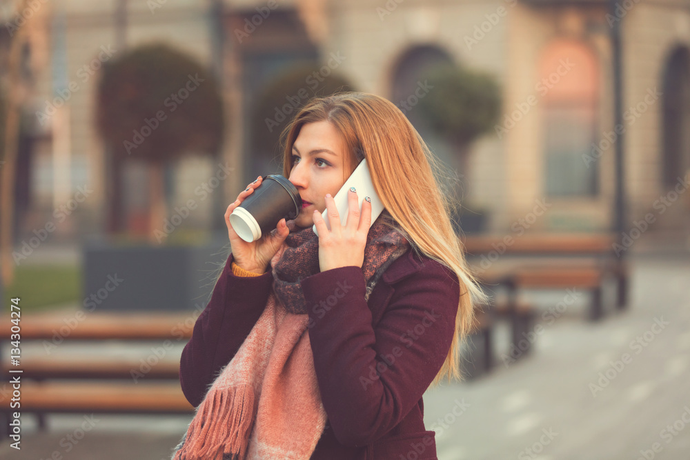 Fototapeta premium Attractive woman using cellphone and drinking coffee outdoors.