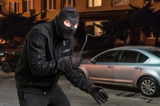 Masked thief in balaclava with crowbar wants to rob a car