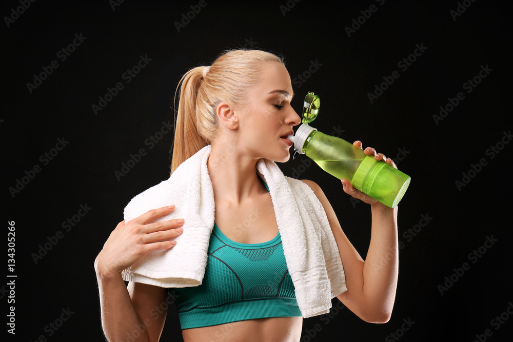 © Africa Studio - Young athletic woman holding bottle with water on black background
