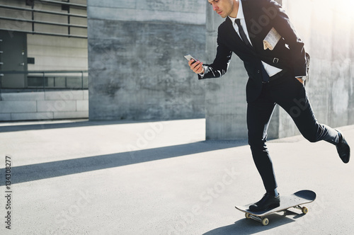 Stylish businessman does skating while holding phone photo