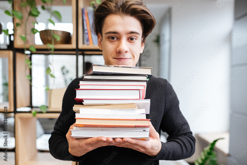 Cheerful student in library holding a lot of books Cheerful student in library holding a lot of books