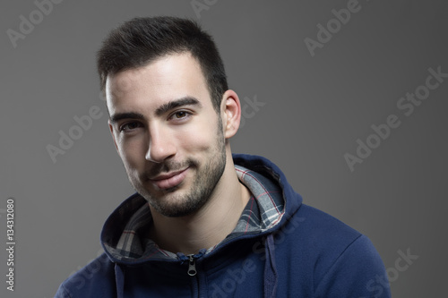 Charming young unshaven man smiling at camera with head slanted. 