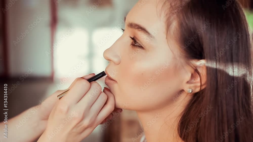 Makeup artist paints lips beautiful young model. Makeup artist paints lips beautiful young model.