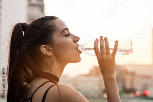 Woman drinking water from bottle. Side view of female face. Little sip of energy.