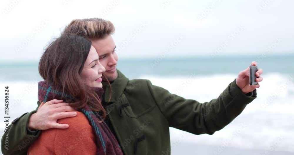 Couple taking selfie on beach in winter Couple taking selfie on beach in winter